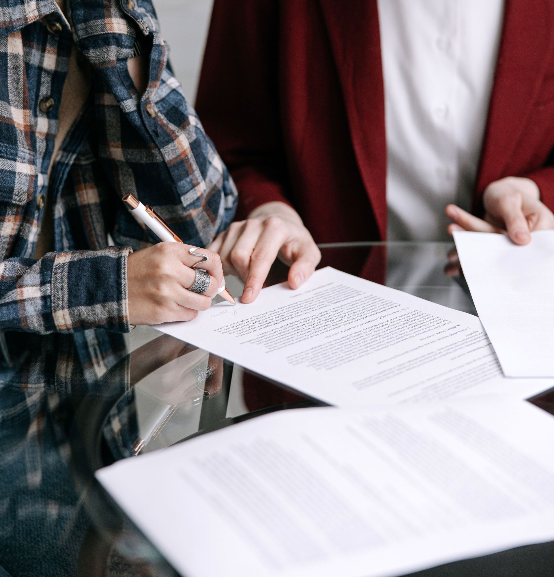 Two women reviewing and signing documents together at a glass table indoors.